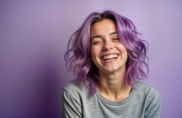 Fototapeta premium Young woman with purple hair smiles happily against purple background. Studio portrait. Beautiful expression. Stylish, cheerful. Modern beauty fashion. Attractive young female model. Fashionable.