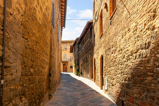 Fototapeta A narrow cobblestone alley in the historic center of the medieval Tuscan hill town of San Gimignano, Italy.