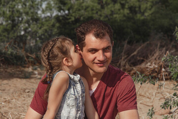 Fototapeta premium little happy daughter whispering in smiling daddy's ear on sunny day