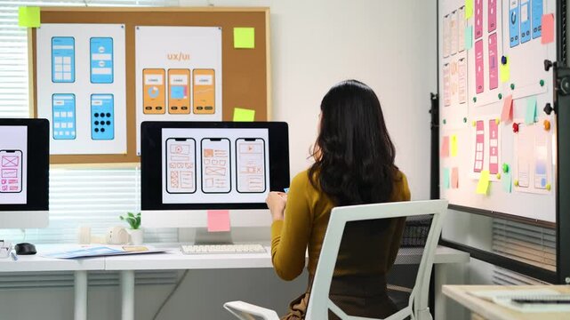 Female ui ux designer working on mobile app design prototype. Ui/ux designer is analyzing the user flow of a mobile application prototype she is designing, using sticky notes on a whiteboard.