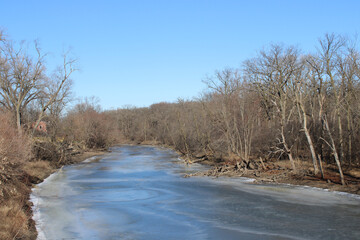 Frozen Des Plaines River with blue ice on a sunny day at Camp Ground Road Woods in Des Plaines, Illinois