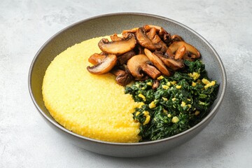 A serving of polenta or corn grits topped with sautéed mushrooms and spinach on a gray dish against a light concrete backdrop Italian recipes