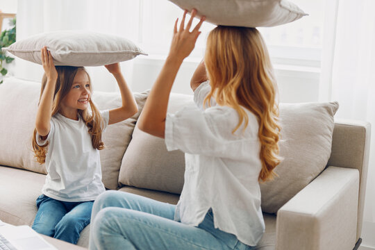 Mother and daughter enjoying a playful moment with pillows on their heads while watching something on a laptop on the couch