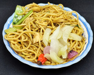 Fried noodles with soy sauce served with pickles, chili, vegetables and meat. Fried noodles with black background.