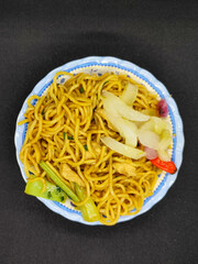 Fried noodles with soy sauce served with pickles, chili, vegetables and meat. Fried noodles with black background.