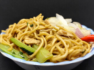 Fried noodles with soy sauce served with pickles, chili, vegetables and meat. Fried noodles with black background.