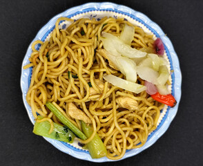 Fried noodles with soy sauce served with pickles, chili, vegetables and meat. Fried noodles with black background.