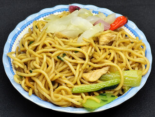 Fried noodles with soy sauce served with pickles, chili, vegetables and meat. Fried noodles with black background.