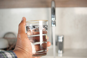 Close-Up of a Hand Holding Glass of Water by a Faucet