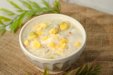 A white bowl of soup with yellow and green pieces of food in it