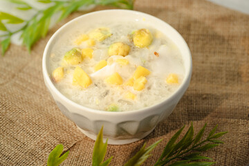 A white bowl of soup with yellow and green pieces of food in it