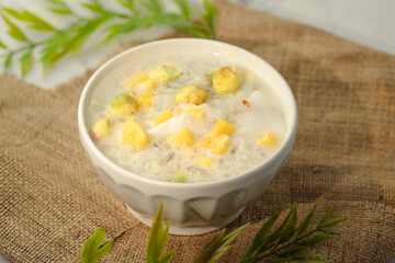 A white bowl of soup with yellow and green pieces of food in it