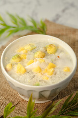 A white bowl of soup with yellow and green pieces of food in it