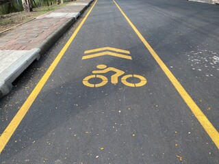 Fototapeta premium Bicycle lane with yellow markings on asphalt in Lumphini Park, Bangkok, promoting cycling and eco-friendly transportation.