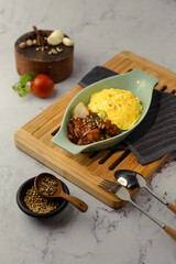 A bowl of food is on a wooden tray with a fork and spoon