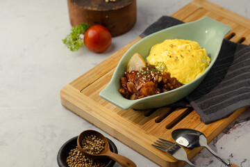 A bowl of food is on a wooden tray with a fork and spoon