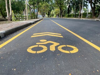Obraz premium Bicycle lane with yellow markings on asphalt in Lumphini Park, Bangkok, promoting cycling and eco-friendly commuting, copy space.