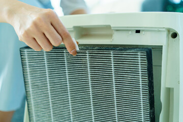 Woman changing air filter, changing a dirty used filter of air purifier machine.