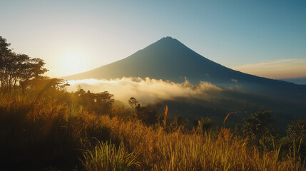 Obraz premium A cone-shaped mountain at sunrise, shrouded in low clouds