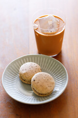 Thai iced tea. Cold drink from Ceylon black tea and milk pouring over ice. Brown orange Ceylon black tea flavor macaron on wooden table.