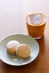 Thai iced tea. Cold drink from Ceylon black tea and milk pouring over ice. Brown orange Ceylon black tea flavor macaron on wooden table.