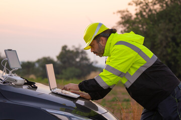 Engineer working on laptop in front of wind turbines for checking wind turbines of the field during beautiful sunset. Alternative energy concept.