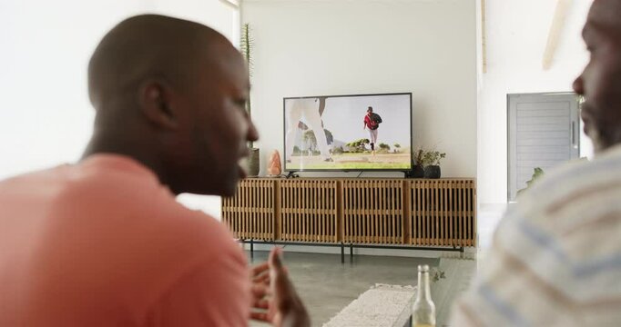Watching baseball game on TV, African American father and son relaxing in living room