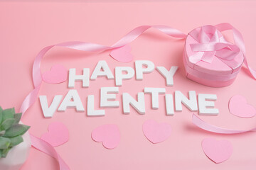 Happy Valentine spelled out with white letters surrounded by pink hearts and ribbon and a pink...