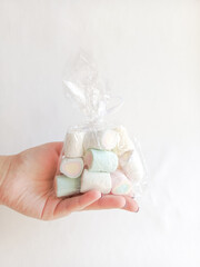 A woman's hand holds a transparent bag with marshmallows on a white background. A sweet gift. Sugar colored marshmallows.