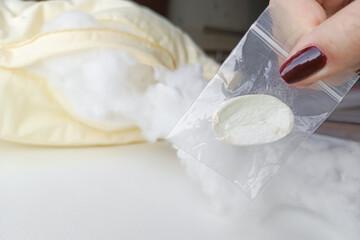 A woman's hand holds a silkworm cocoon in a ZIP bag, with a yellow silk pillow filled with silkworm threads in the background.