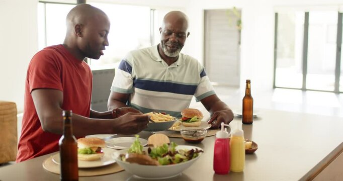 Eating lunch together, African american father and adult son enjoying burgers and fries at home
