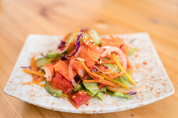 Colorful mixed vegetable salad with vibrant toppings served on a decorative plate over a wooden table.