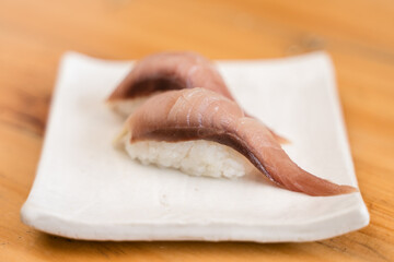 Two pieces of shima aji (striped jack) sushi placed on a minimalist white ceramic plate over a wooden table.