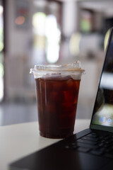 Iced black coffee in a plastic cup with computer notebook in the cafe