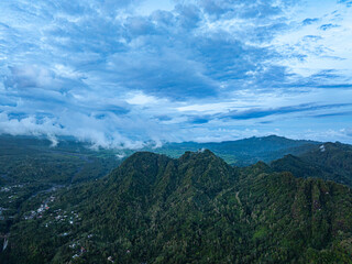Aerial view Kabut Pelangi Waterfall in East Java. The waterfall stream flows into the mountain gorge in a long path.Above is the residence of the villagers. Abundance of forests on the green mountain.
