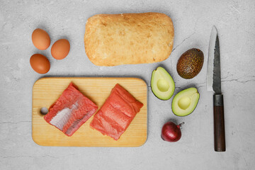Top view of ingredients for cooking sandwiches with salmon fillets including bread, eggs, avocado, and red onion
