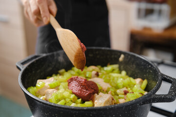 Cooking celery and meat with tomato paste in a pot during meal preparation in a kitchen
