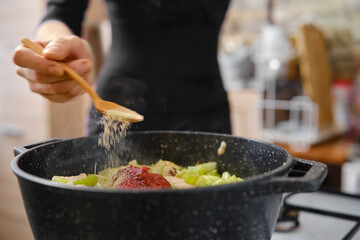 Sprinkling spice over vegetables in a black pot while preparing a hearty meal