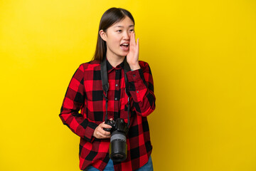 Young photographer Chinese woman isolated on yellow background shouting with mouth wide open to the lateral