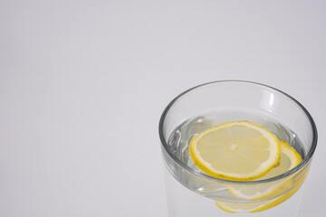 A minimalist close up of lemon slices in a glass of water on a white surface. The simplicity conveys freshness and detox themes, suitable for wellness campaigns or hydration related posts