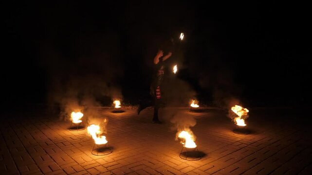 A young brunette is dancing with fire, creating a show with lights on a dark background. An outdoor circus performance at night. A woman turns burning torches in her hands. An amazing fire show.