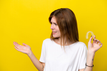 Young English woman holding invisible braces with surprise expression while looking side