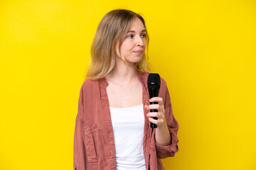 Young singer caucasian woman picking up a microphone isolated on yellow background looking to the...