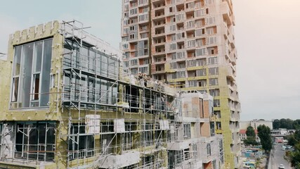 Construction progress of a new high-rise building in downtown area during summer with workers on scaffolding