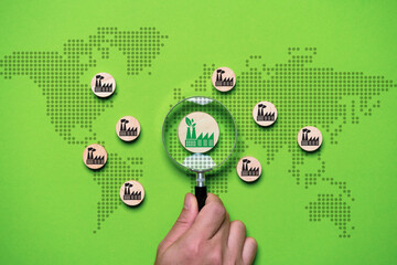 Hand holding magnifier glass with green factory among black pollution with map for green economy to...