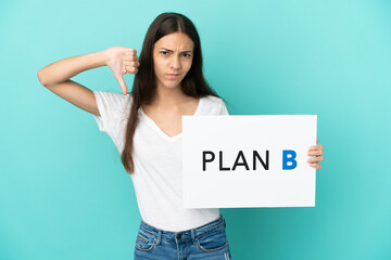 Young French woman isolated on blue background holding a placard with the message PLAN B and doing...