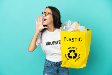 Young French girl holding a bag full of plastic bottles to recycle shouting with mouth wide open to...