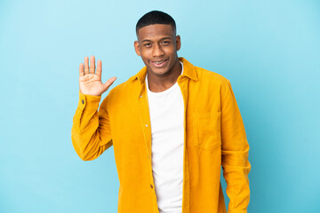 Young latin man isolated on blue background saluting with hand with happy expression