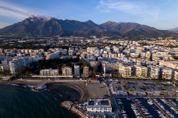 Marbella luxury yacht sports port with boulevard and historic city center in the background and La Concha mountain rising above in blue sky during sunset. Aerial Andalusian sun coast of Spain