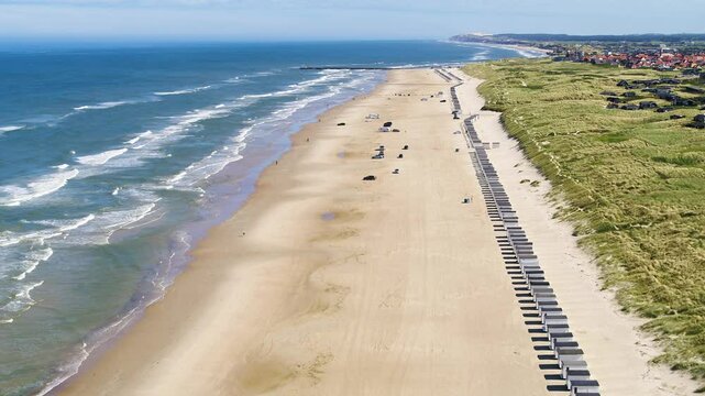 Drone flying forwards over beach with long row of beach huts